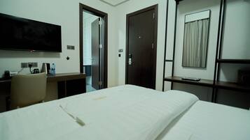 A hotel room with a bed, a desk with a chair, a flat-screen TV, and a wardrobe.