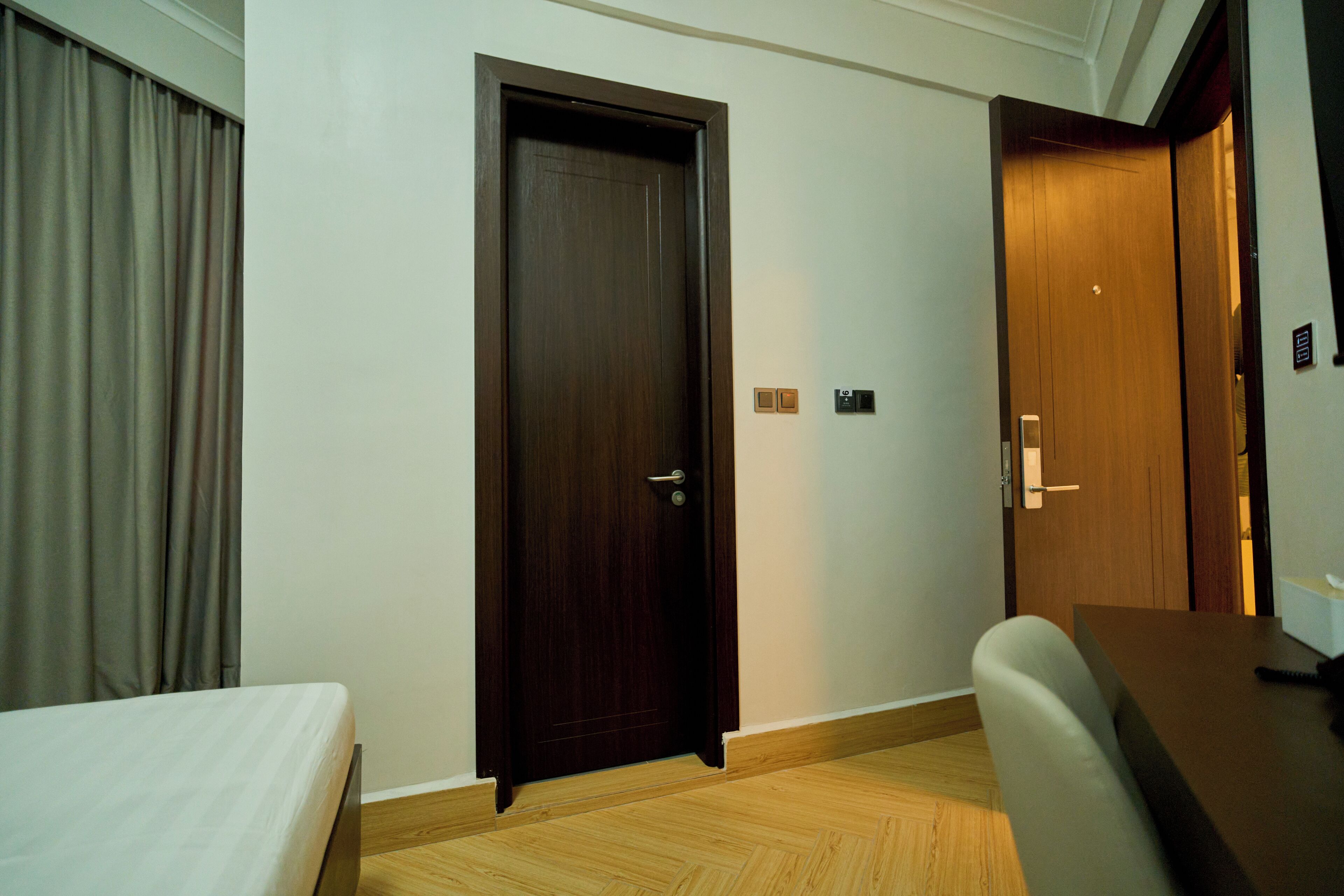 A hotel room with a wooden door, a bed, a desk, and a chair.