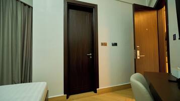 A hotel room with a wooden door, a bed, a desk, and a chair.