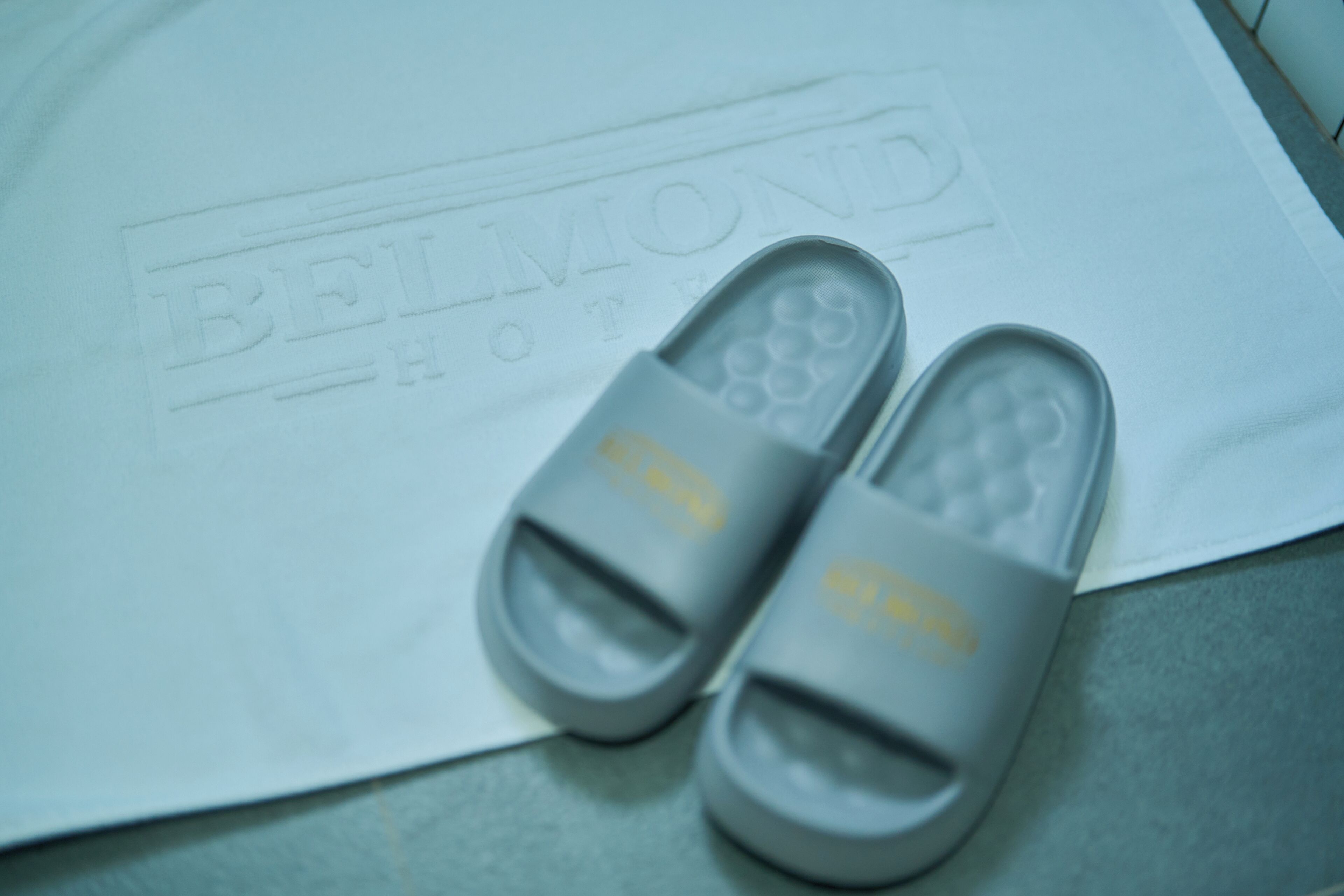 A pair of grey slippers with a logo on a white surface with embossed text.