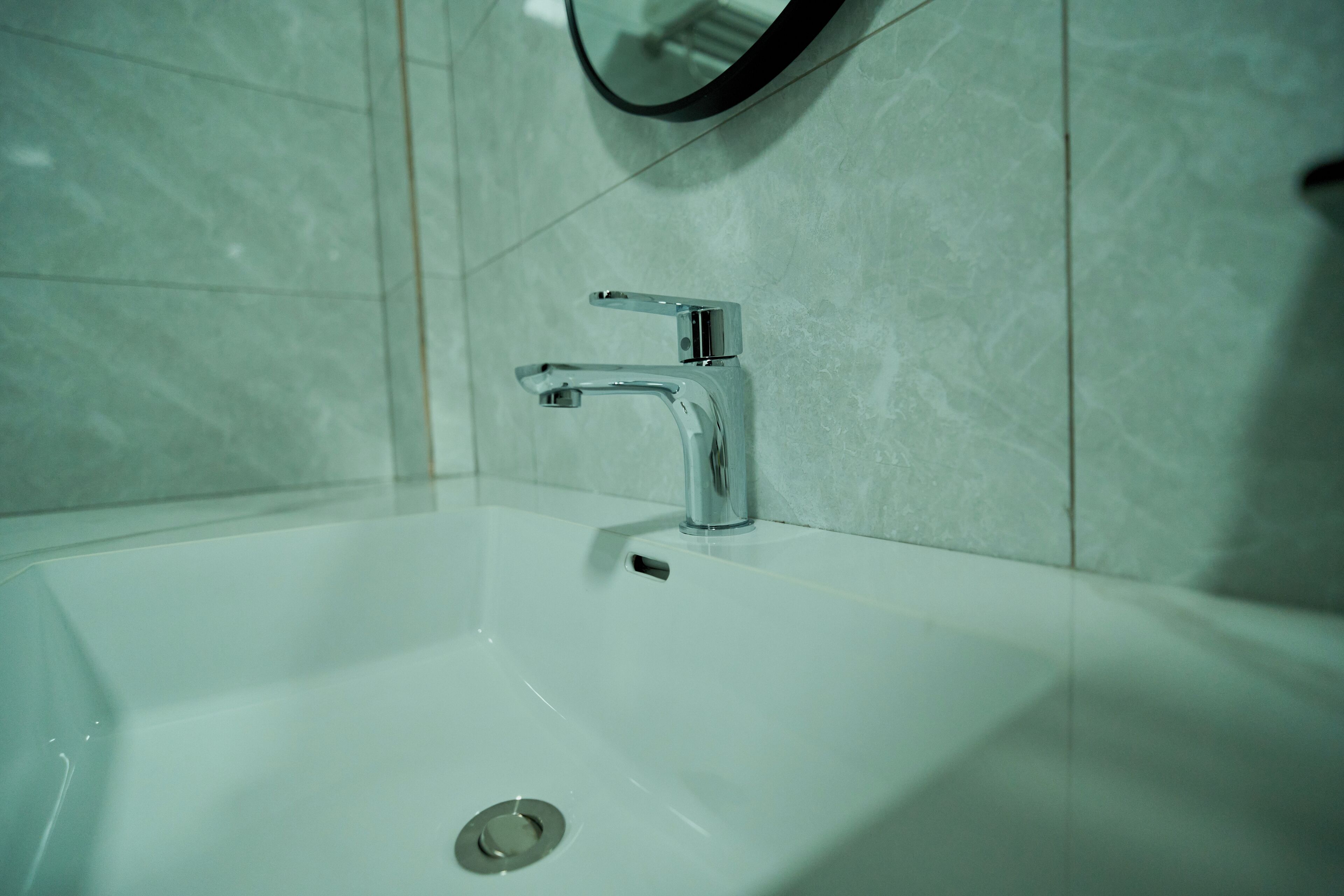 Een badkamer met een witte wastafel, chromen kraan en een ronde spiegel aan de muur.