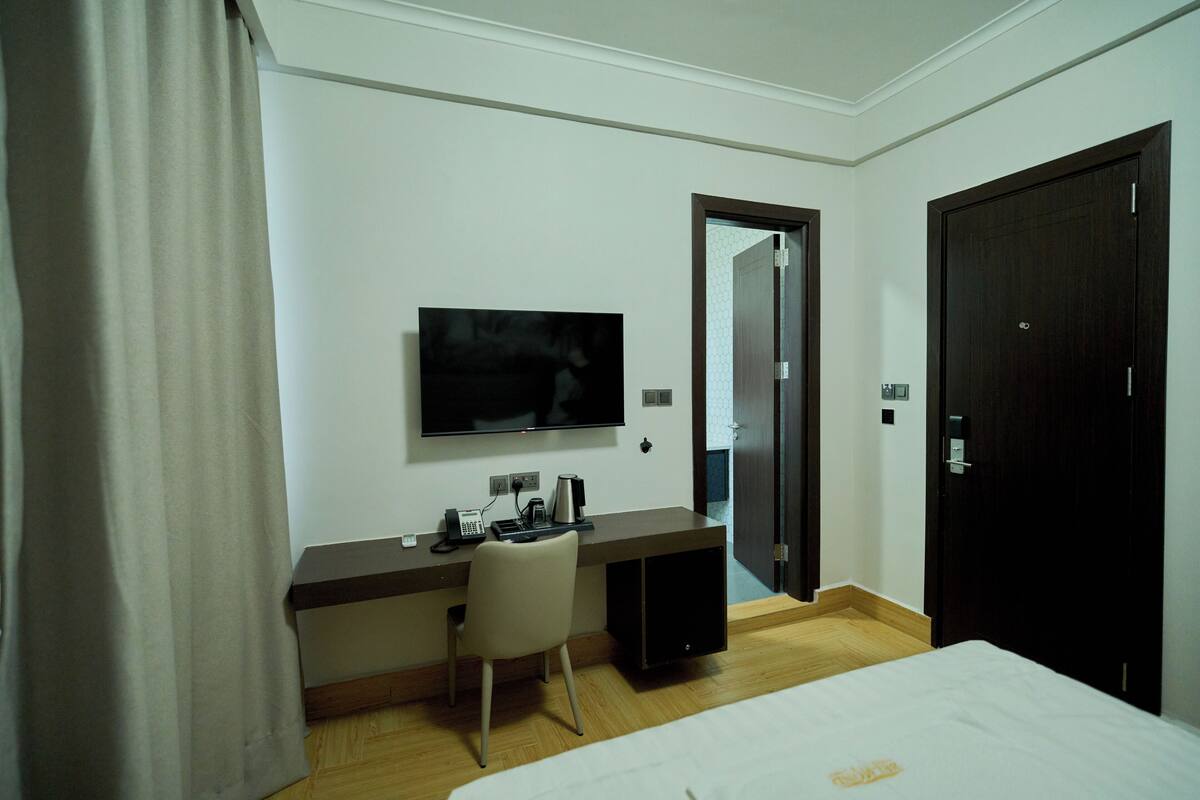 Een hotelkamer met een bed, een bureau met stoel, een televisie en een deur.