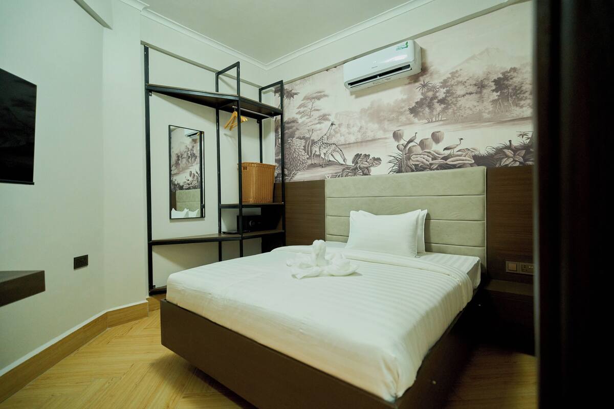 Een hotelkamer met een bed, een wandplank met een mand, en een muurschildering van een landschap.