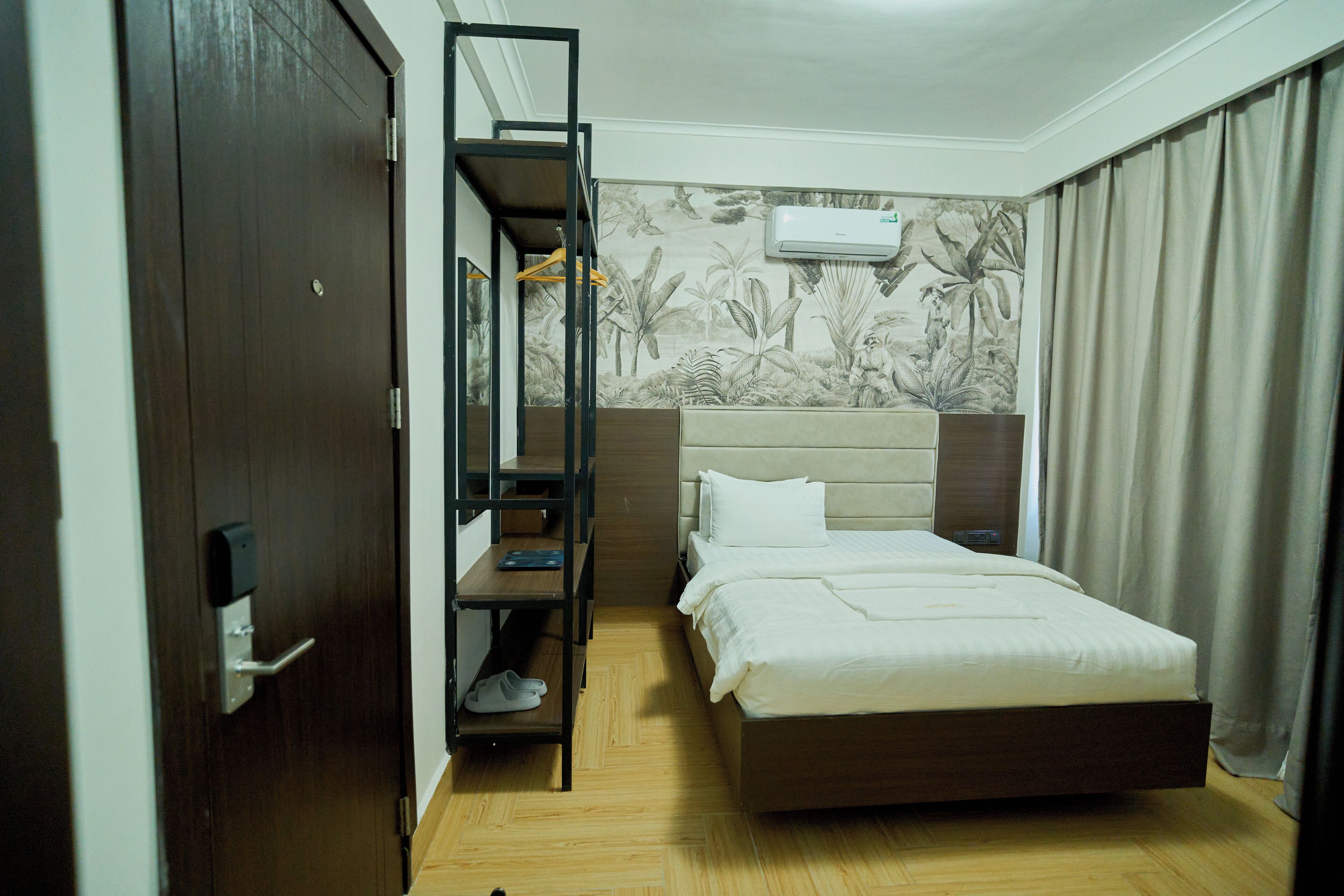 Quarto de hotel com cama, guarda-roupa, prateleira com sapatos e ar-condicionado fixado na parede.