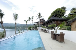 An infinity pool with a view of the sea and mountains, lounge chairs, and a wooden building with a thatched roof. - Villa De Pico Highland Beach Resort (Puerto Galera)