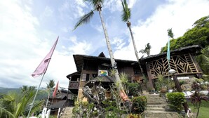 A traditional wooden building with a thatched roof, surrounded by lush greenery and palm trees. - Villa De Pico Highland Beach Resort (Puerto Galera)