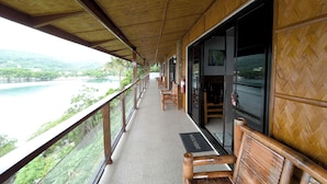 A wooden balcony with a view of a lake and mountains, wooden chairs, and a welcome mat. - Villa De Pico Highland Beach Resort (Puerto Galera)