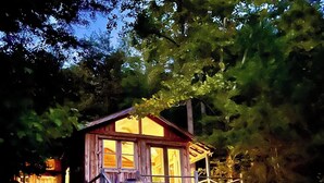 A wooden cabin with a porch and a staircase leading up to it, surrounded by trees. - Whimsical Wildwood Studio – Breakfast Included – Award-Winning Appalachian B&B (Irvine)