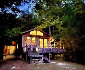 A wooden cabin with a porch and a staircase leading up to it, surrounded by trees. - Whimsical Wildwood Studio – Breakfast Included – Award-Winning Appalachian B&B (Irvine)