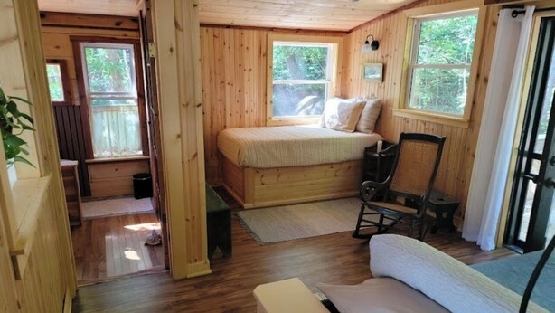 A wooden cabin with a bed, a chair, and a small table. - Whimsical Wildwood Studio – Breakfast Included – Award-Winning Appalachian B&B (Irvine)