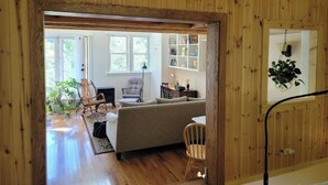 A cozy living room with a sofa, chairs, and a dining table. There is a wooden ceiling and a view of the outdoors through a large window. - Whimsical Wildwood Studio – Breakfast Included – Award-Winning Appalachian B&B (Irvine)