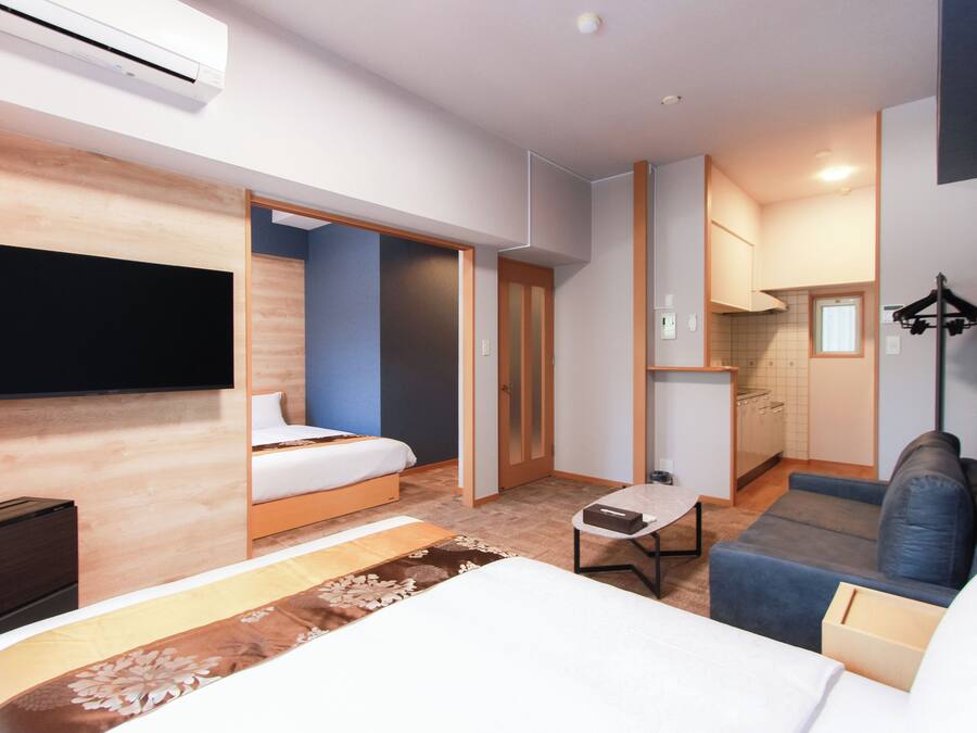 Quarto de hotel moderno com cama, sofá, mesinha e televisão.