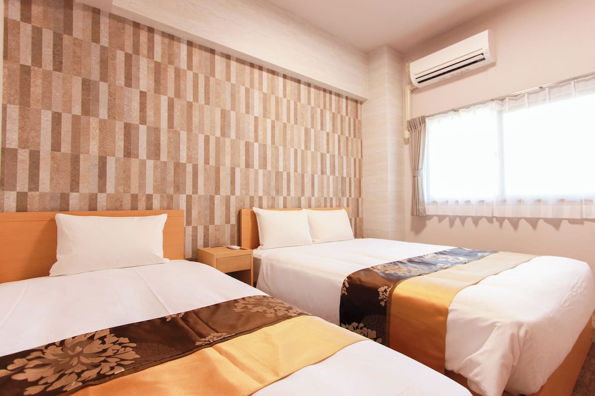 Ein Hotelzimmer mit zwei Betten, einer karierten Wand, einer Klimaanlage und einem Fenster mit Vorhängen.