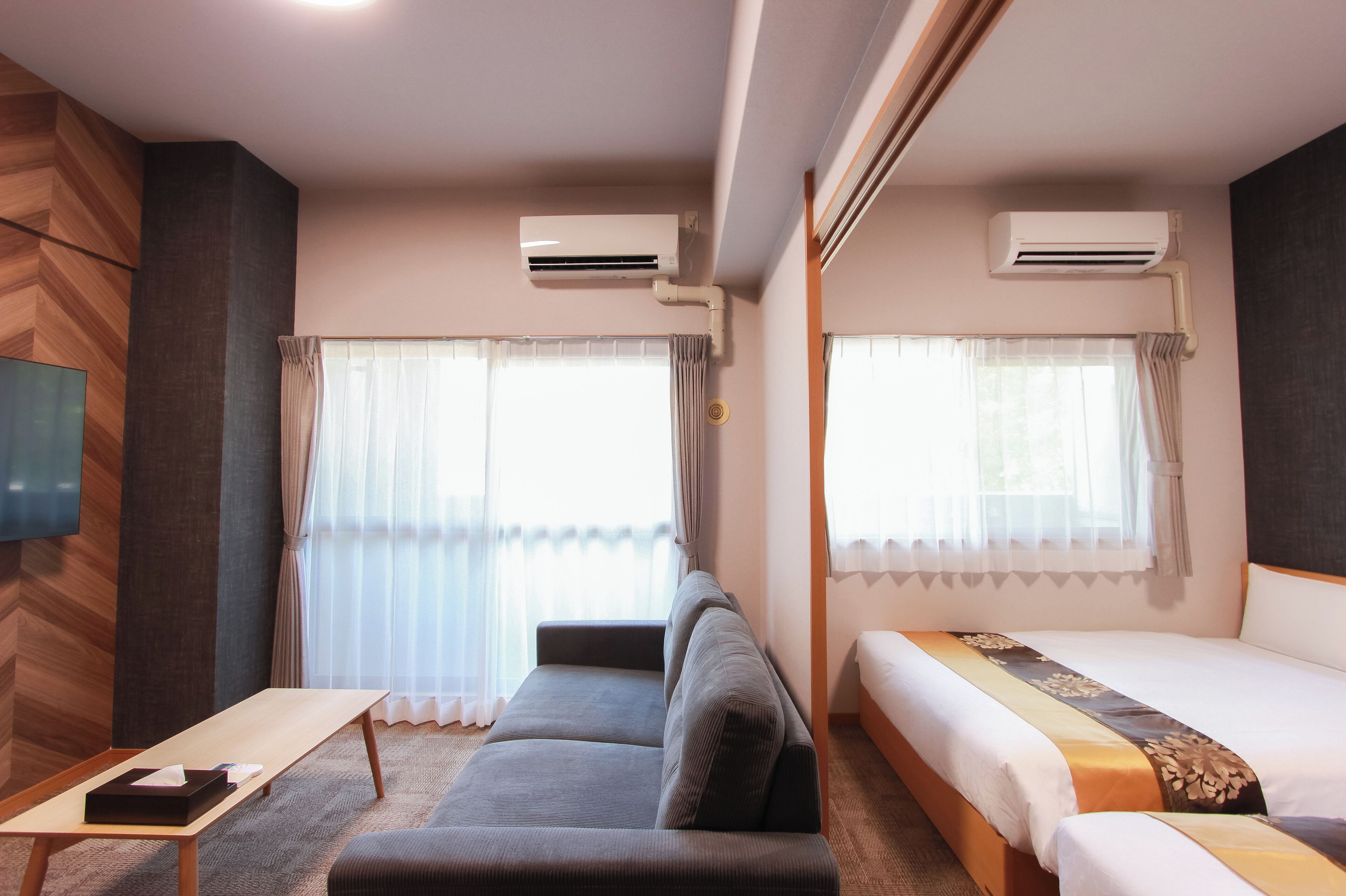 A hotel room with a sofa, a bed, and an air conditioning unit.