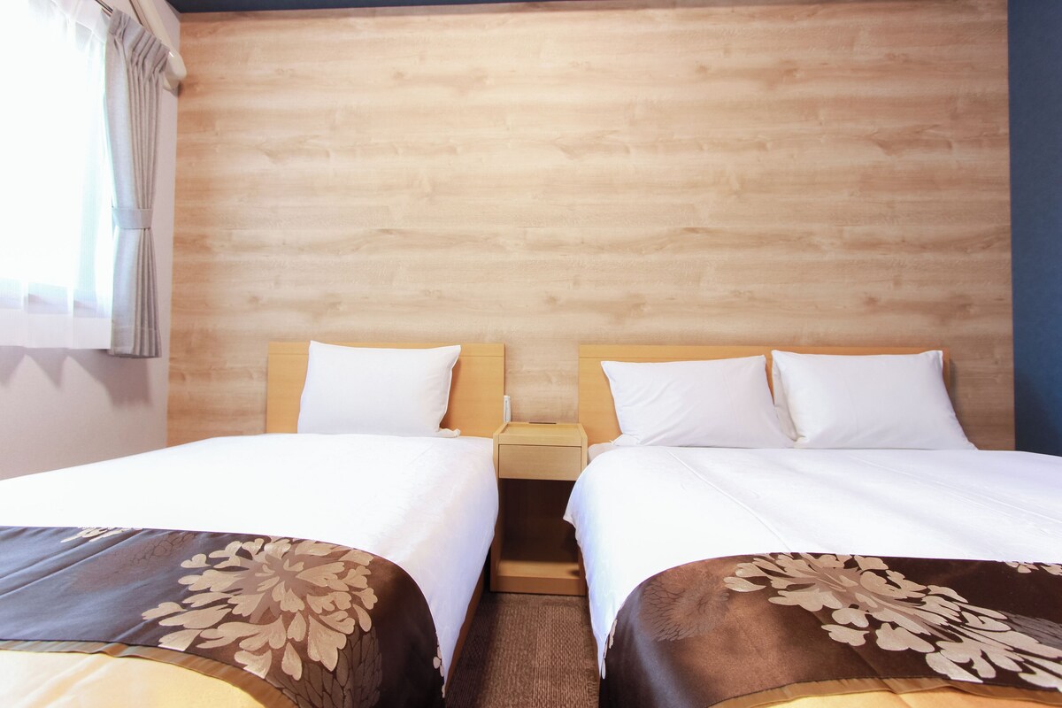 Una habitación de hotel con dos camas individuales, cabeceros de madera y una mesita de noche entre ellas.