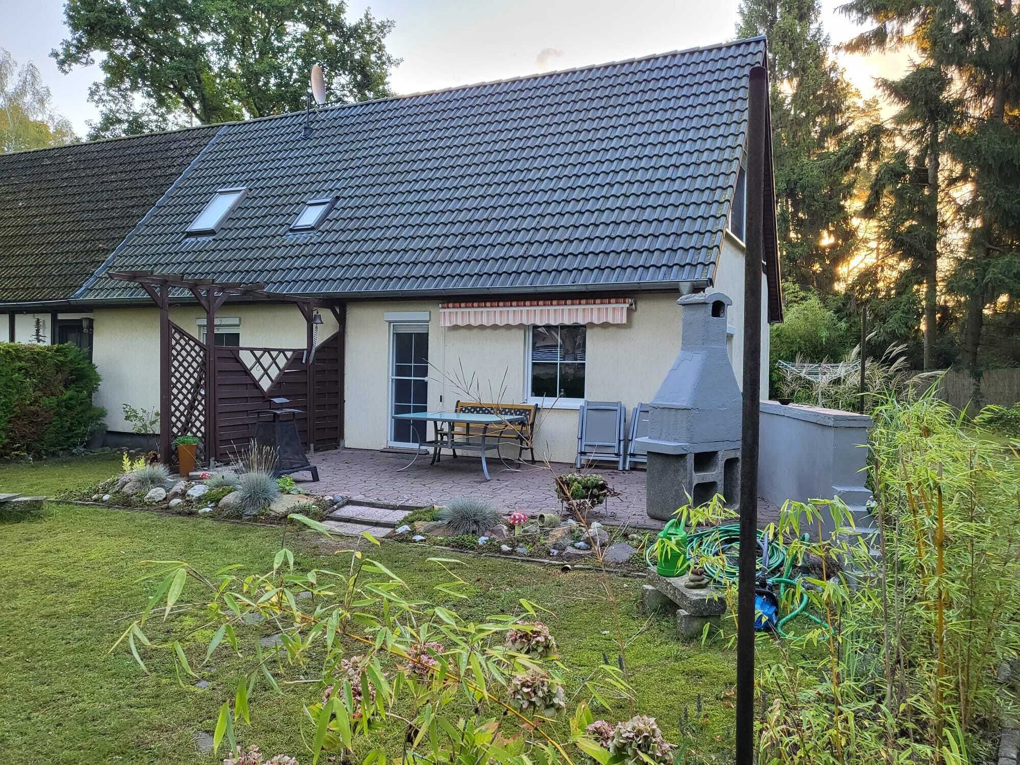Uma casa com telhado de telhas, um pátio com mesa e cadeiras, e um jardim com diversas plantas.