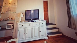 Habitació petita i acollidora amb un armari blanc, una televisió i una làmpada. Hi ha una porta de fusta i una finestra amb cortines.
