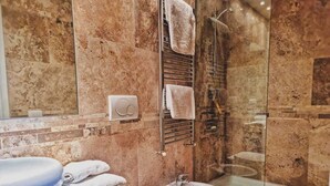 Un bany amb paret de marbre, box de dutxa de vidre, vàter, bidet i rentapès.