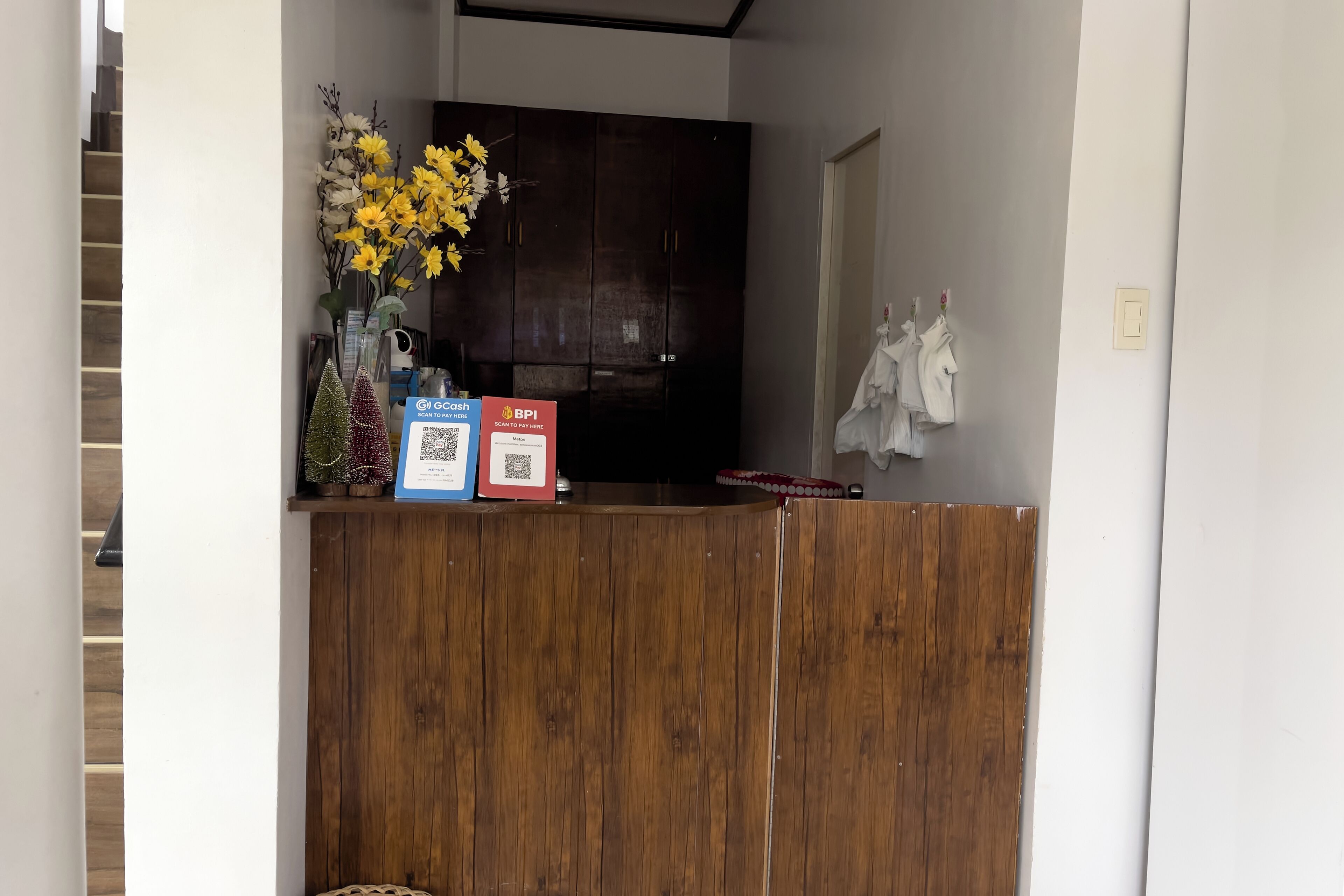 A reception desk with a wooden finish, a vase with yellow flowers, and two QR codes for payment options.