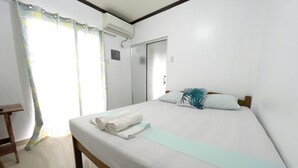 A hotel room with a bed, a wooden nightstand, a window with curtains, and an air conditioning unit.