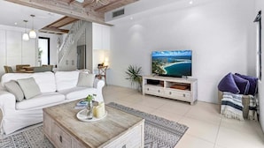 A modern living room with a white sofa, a wooden coffee table, and a TV on a white stand. - Riverside Haven, Noosa Heads (Noosa Heads)