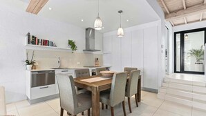 A modern kitchen with white cabinetry, a wooden dining table, and pendant lighting. - Riverside Haven, Noosa Heads (Noosa Heads)