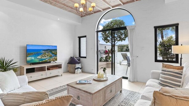 A spacious living room with a television, comfortable seating, a coffee table, and a large window offering a view of the outdoors. - Riverside Haven, Noosa Heads (Noosa Heads)