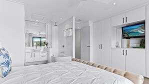 A modern bedroom with a large bed, a TV, and a bathroom with a bathtub and shower. - Riverside Haven, Noosa Heads (Noosa Heads)