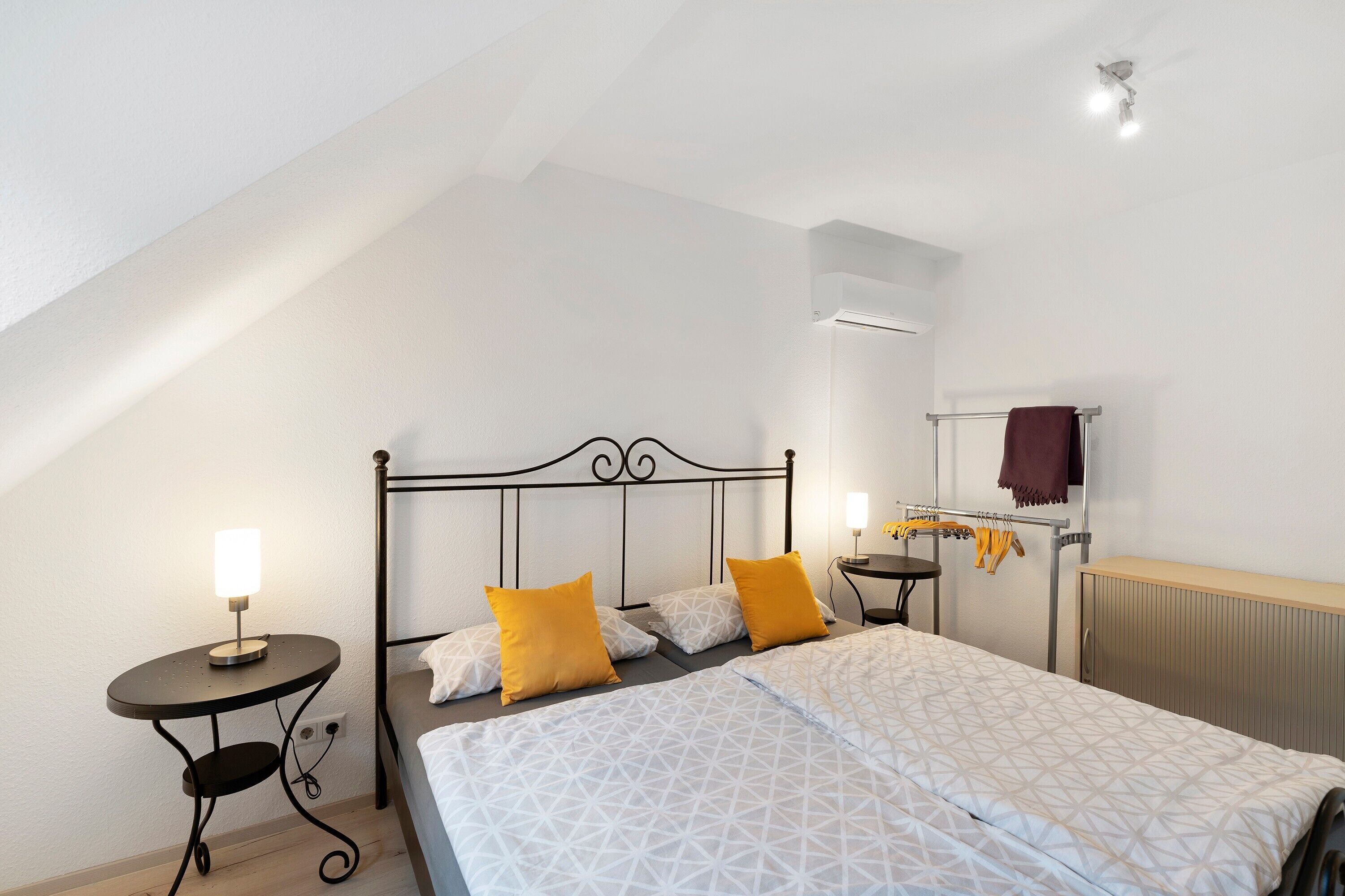 A bedroom with a bed, two bedside tables, a wall-mounted heater, and a ceiling fan.