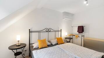 A bedroom with a bed, two bedside tables, a wall-mounted heater, and a ceiling fan.