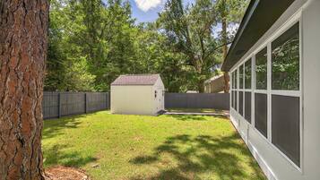 A backyard with a small shed, a wooden fence, and a house with large windows.