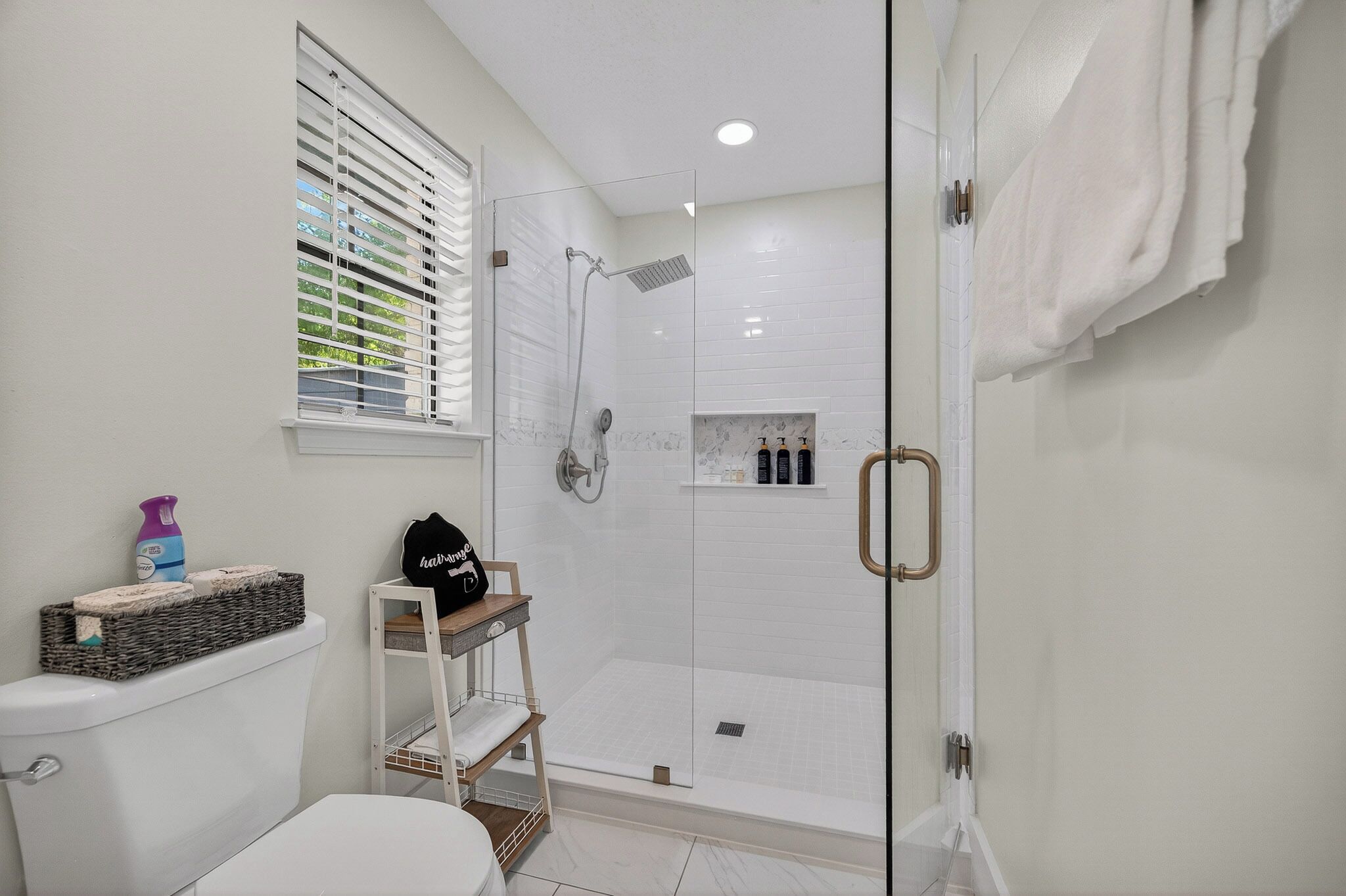 A modern bathroom with a glass shower enclosure, a toilet, a sink, and a window with blinds.