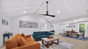 A spacious living room with a blue sofa, orange armchair, and a coffee table. There are framed pictures on the walls and a ceiling fan. - The Skipper’s Hideaway: Golf Course & Pool Oasis (Daphne)
