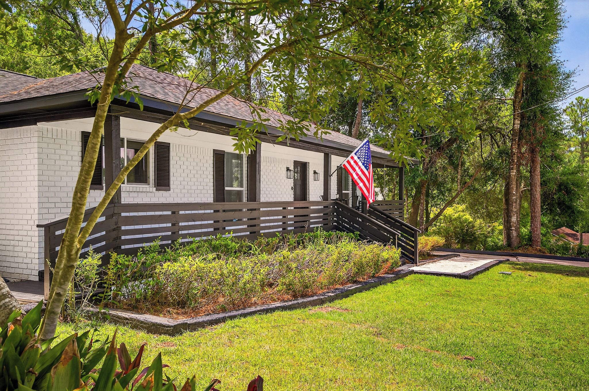 A white brick building with a black roof, a wooden fence, and an American flag.