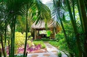 A tropical garden pathway leading to a thatched-roof structure with seating.
