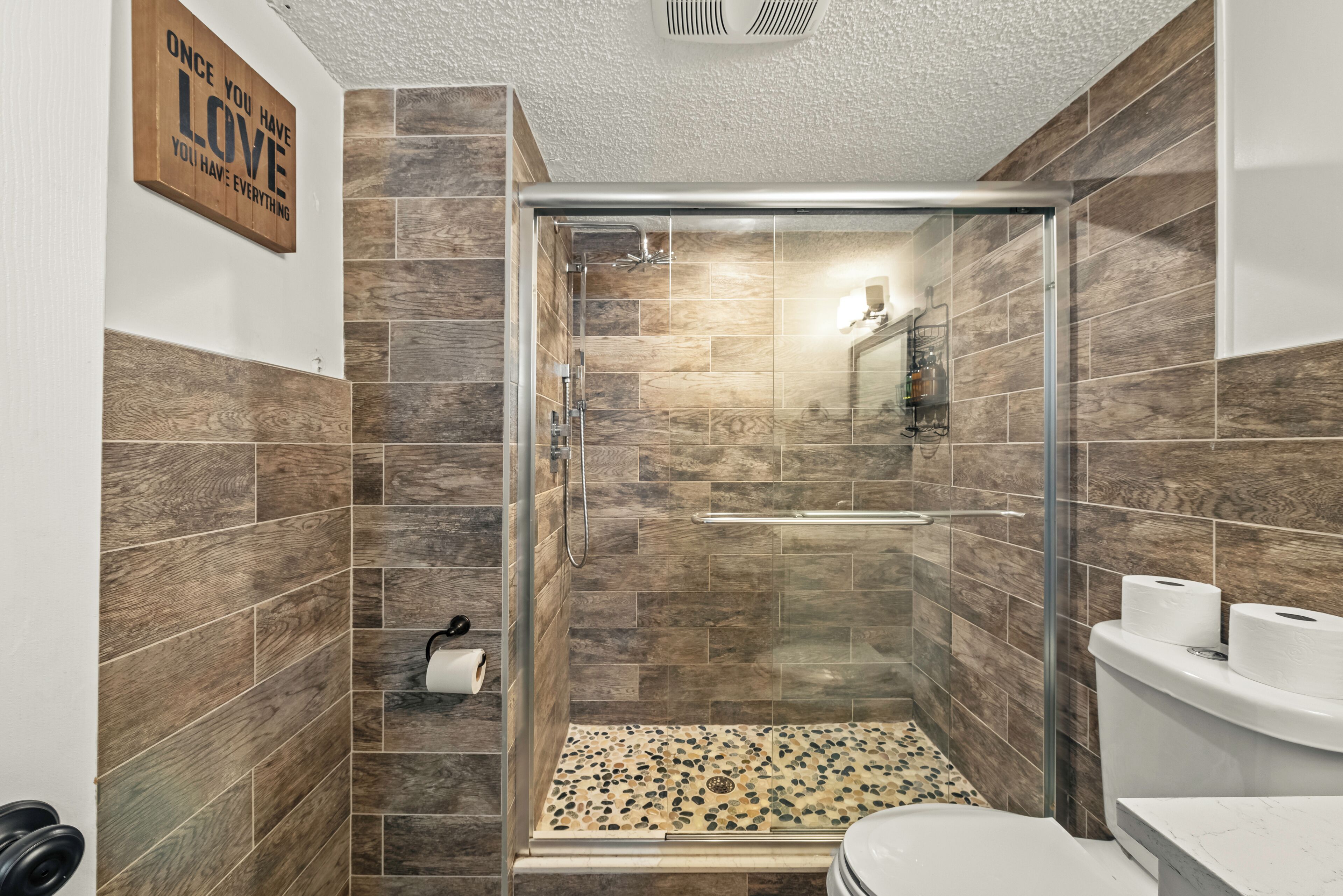 Un baño moderno con ducha de vidrio, revestimiento de madera en las paredes y un inodoro con dos rollos de papel higiénico.