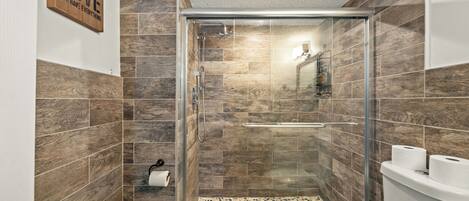 Un baño moderno con ducha de vidrio, revestimiento de madera en las paredes y un inodoro con dos rollos de papel higiénico.