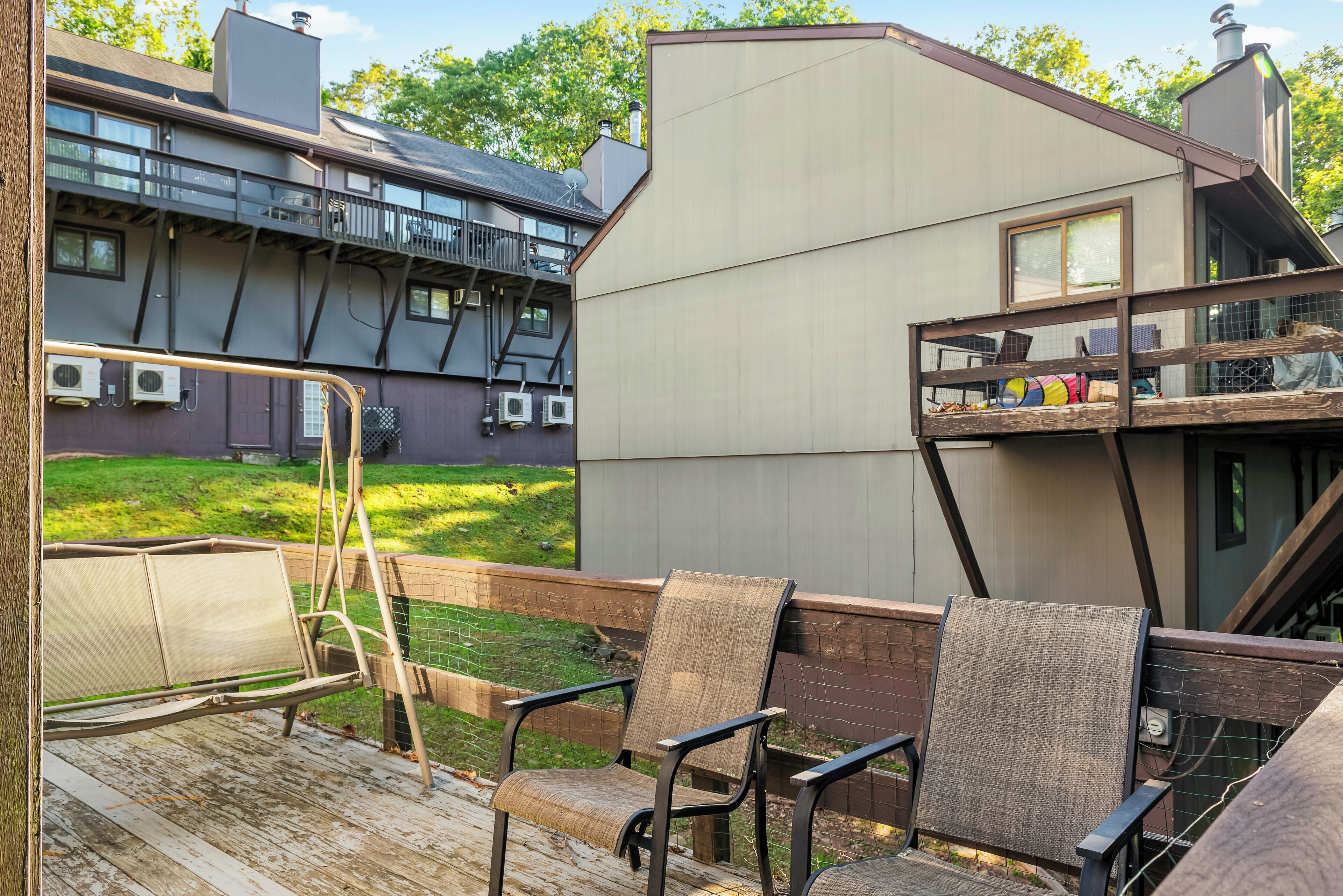 A deck with outdoor furniture, a wooden railing, and a view of a modern house with a balcony.