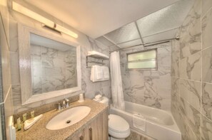 A bathroom with a marble-tiled wall, a sink with a granite countertop, a toilet, and a bathtub. - Work & Waves: Gold Coast 2BR Escape (Pompano Beach)
