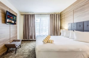 A hotel room with a bed, a TV mounted on the wall, a chair, and a window with curtains. - Riverside Vacation Rentals by Rocketstay (Pompano Beach)