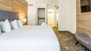 A hotel room with a large bed, a bedside table with a lamp, a wardrobe, and a seating area with a chair.