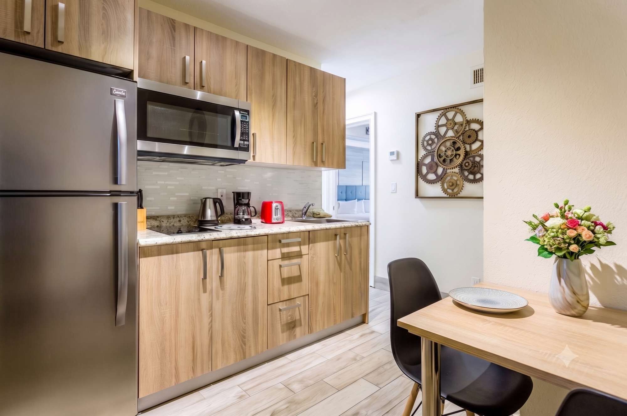 A compact kitchen with a refrigerator, microwave, coffee maker, and toaster. There's a dining area with a table and chairs.