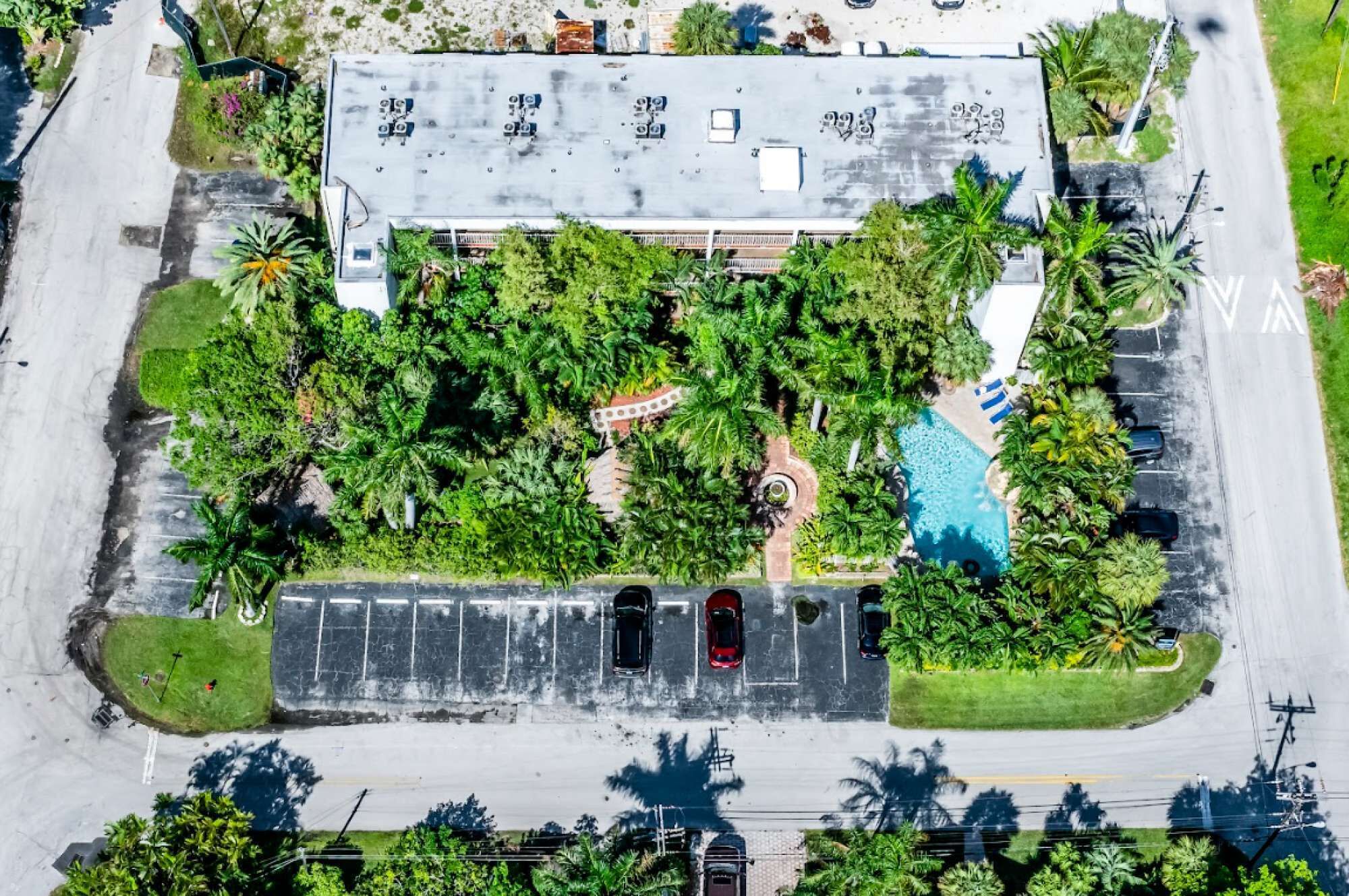 Vue aérienne d’un parking avec une piscine, entouré d’une végétation luxuriante et de palmiers.