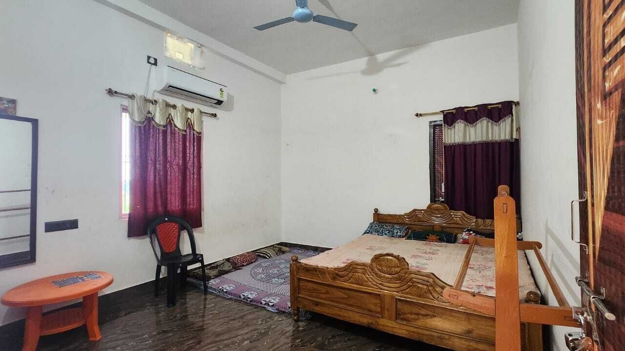 Een slaapkamer met een houten bed, een stoel, een airconditioning en een raam met gordijnen.