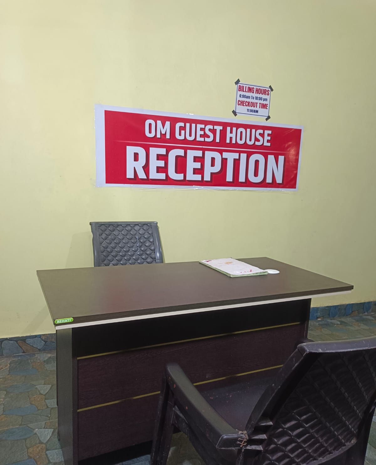 A reception desk with a sign indicating 'OM GUEST HOUSE RECEPTION' and 'BILLING HOURS 6:00am to 10:00pm' and 'CHECKOUT TIME 11:00am'.