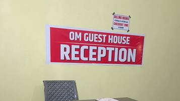 A reception desk with a sign indicating 'OM GUEST HOUSE RECEPTION' and 'BILLING HOURS 6:00am to 10:00pm' and 'CHECKOUT TIME 11:00am'.