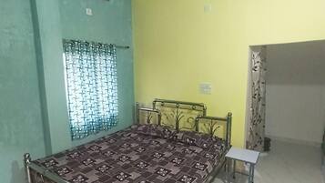 A bedroom with a bed, a ceiling fan, a window with patterned curtains, and a small table.