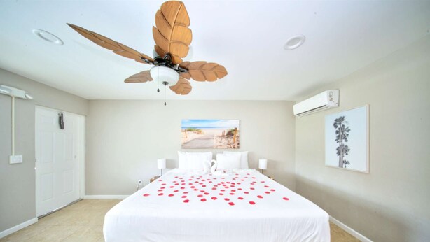 A hotel room with a bed, a ceiling fan, a beach view poster, and an air conditioning unit.