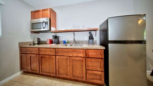 A kitchen with wooden cabinets, a stainless steel refrigerator, a microwave, and a coffee maker. - Sun Soaked in Paradise - King Studio W/ Pool (Pompano Beach)