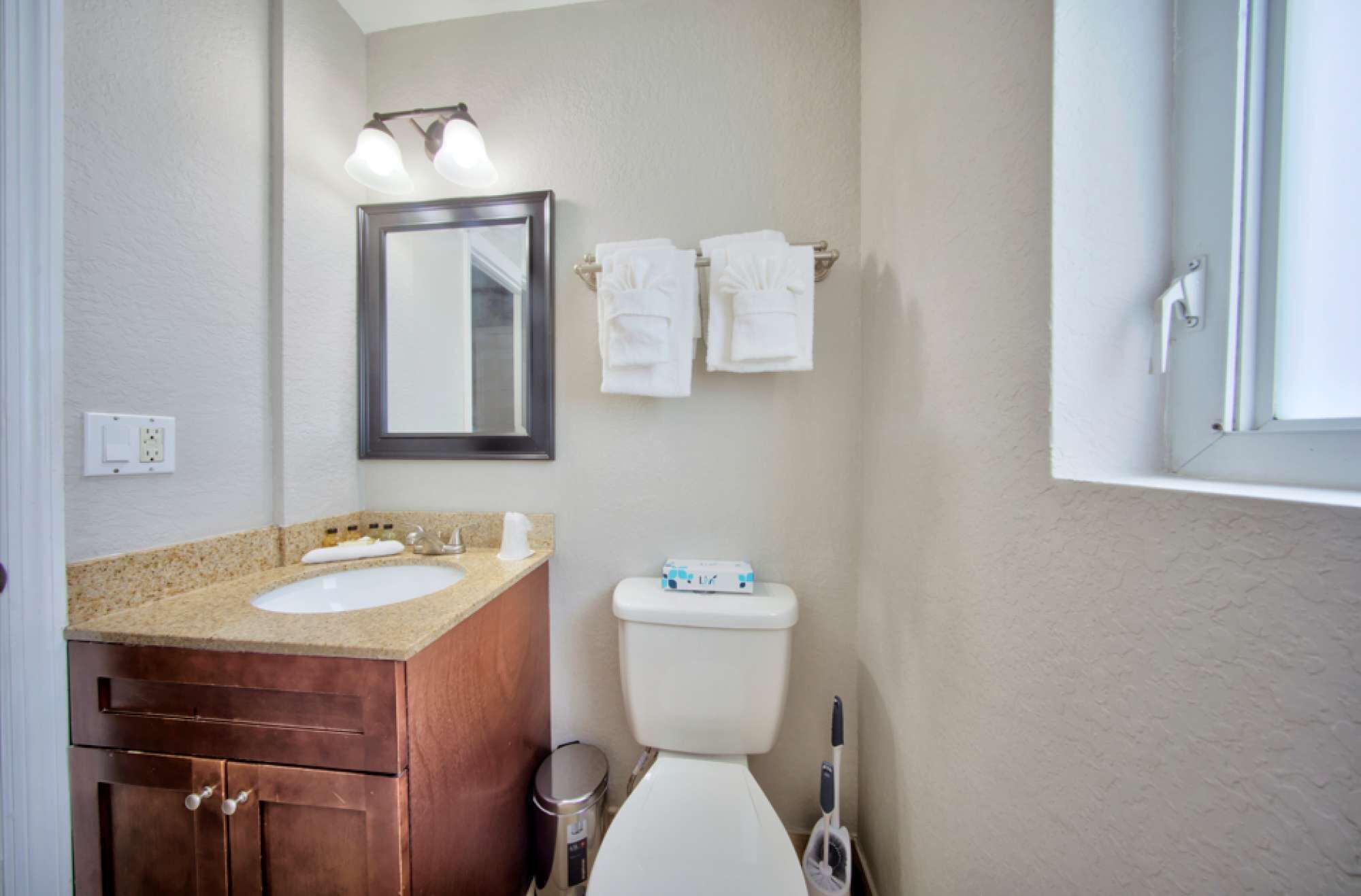 Een badkamer met een dubbele wastafel, toilet, spiegel en een handdoekrek met handdoeken.